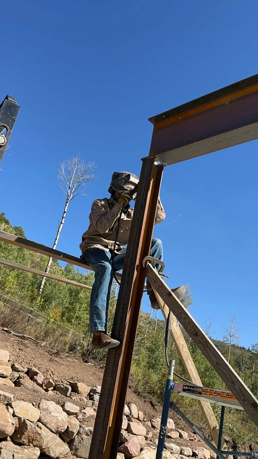 Welder up on a ladder, welding a steel beam frame against a blue sky